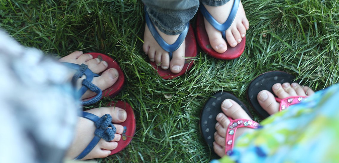 Photo of 3 kids feet in flip flops.