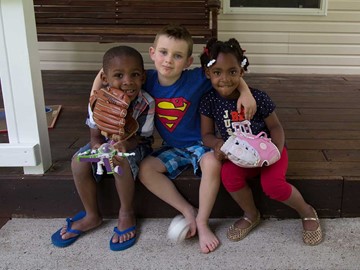 3 kids sitting on a porch with one holding a baseball mit