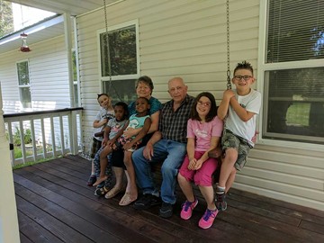 Great grandparents on a bench on a porch with great grand-kids.