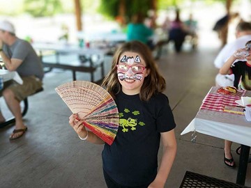 Large holding a fan with her face painted