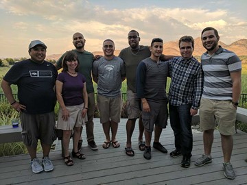 8 people standing on a deck in a backyard.