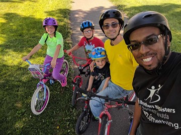 2 adults and 3 kids on bikes in a park
